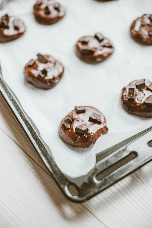 a pan filled with chocolate covered cookies on top of a table, by Nicolette Macnamara, unsplash, on a pale background, oven, caramel. rugged, lily pads