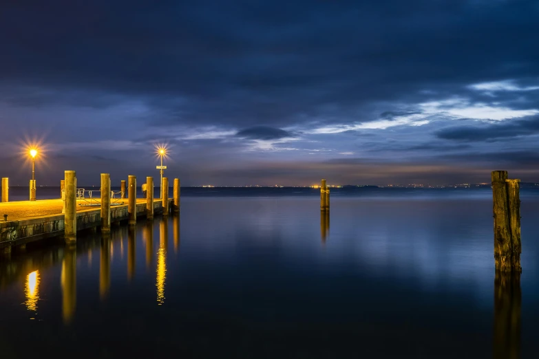a pier next to a body of water at night, by Peter Churcher, golden and blue hour, port, slight overcast, landscape photo
