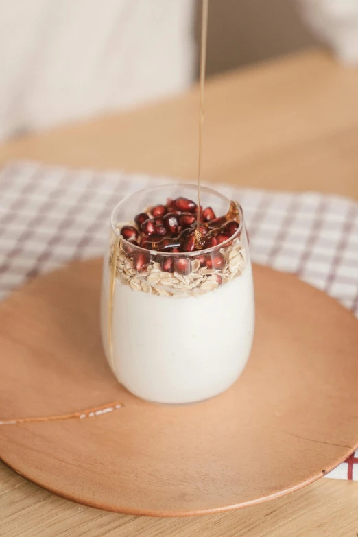 a close up of a glass of yogurt on a plate, by Nicolette Macnamara, trending on pexels, big oatmeal, pomegranate, square, malt