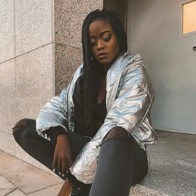 a woman sitting on the steps of a building, an album cover, trending on pexels, silver metallic moncler jacket, ( ( dark skin ) ), thinking pose, bomber jacket