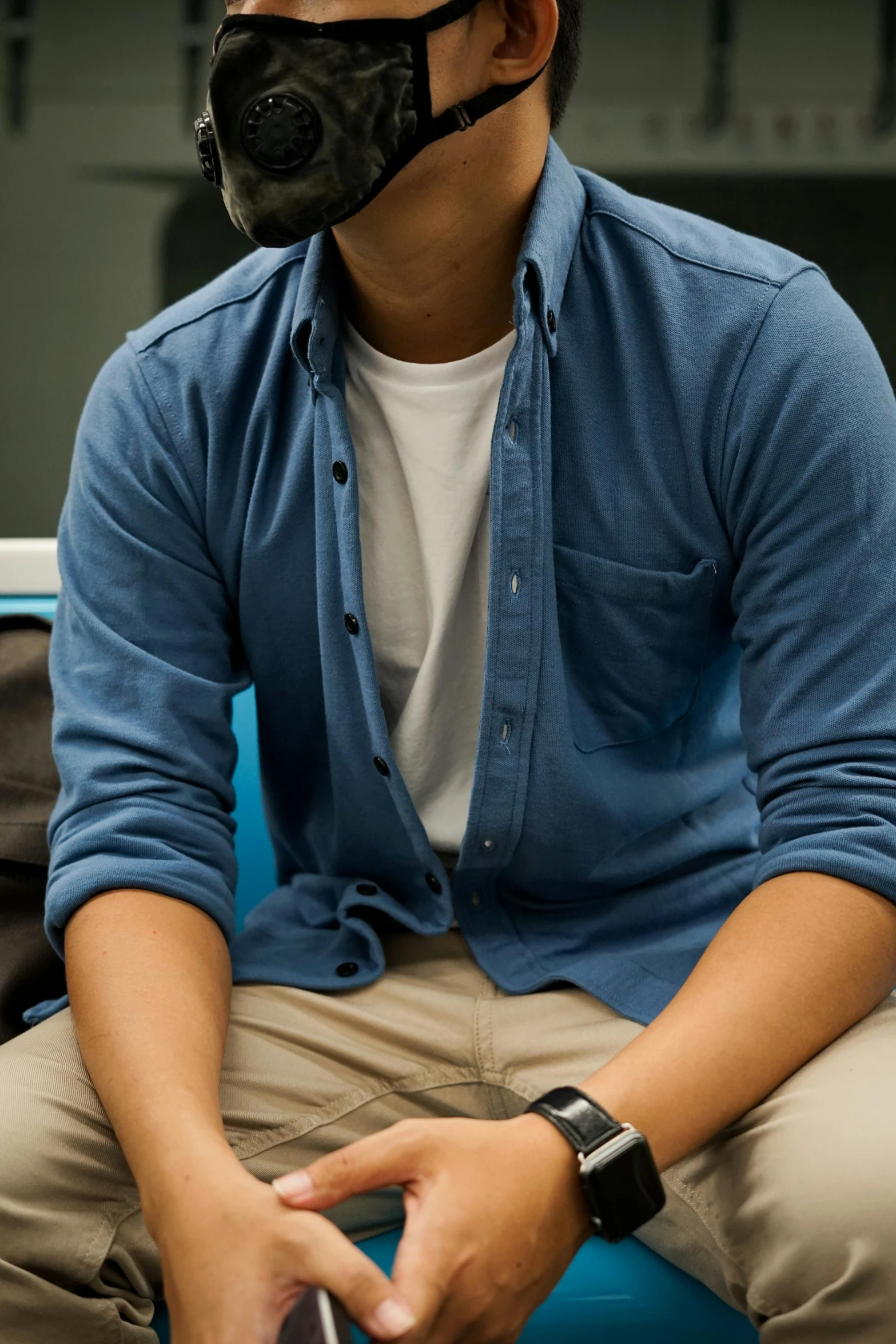 a man wearing a gas mask sitting on a blue chair, by Robbie Trevino, trending on unsplash, button - up shirt, student, khakis, blue soft details