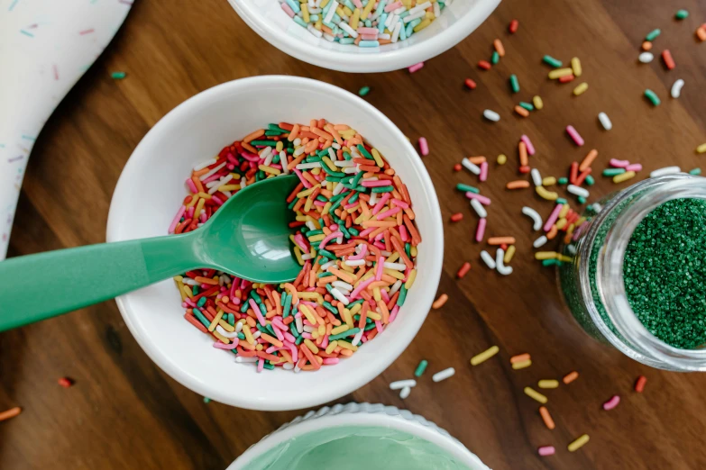 a wooden table topped with bowls filled with sprinkles, trending on pexels, spatula, turquoise pink and green, thumbnail, pouring