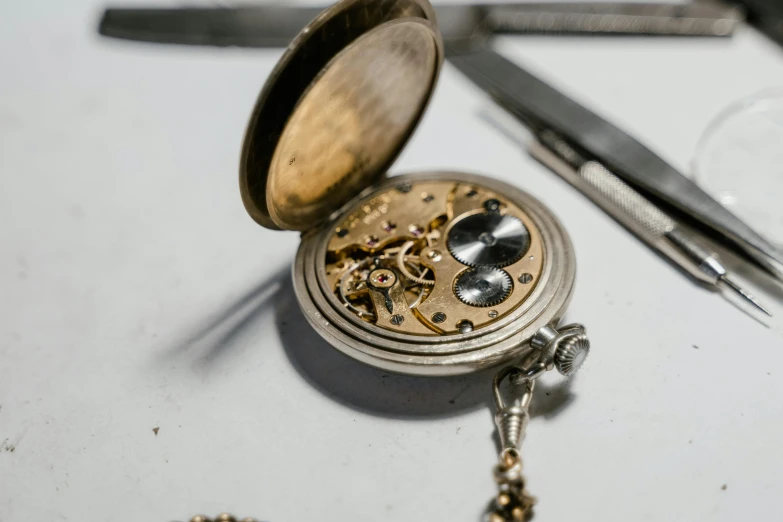 a close up of a pocket watch on a table, by Matija Jama, trending on pexels, assemblage, in a workshop, cut-away, platinum jewellery, manufactured in the 1920s