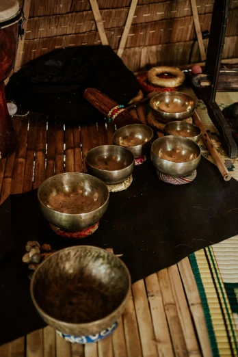 a group of metal bowls sitting on top of a wooden floor, inspired by Gong Kai, hurufiyya, tribal clothing, coffee, - 8, multiple stories