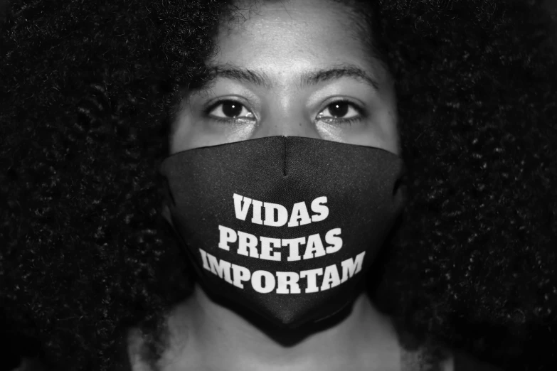 a woman wearing a face mask that says vidas pretass important, a black and white photo, by Almada Negreiros, pexels, afro, brasil, vantablack gi, empty eyes