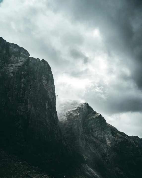 a person standing on top of a mountain under a cloudy sky, pexels contest winner, minimalism, ominous dark background, sharp cliffs, it's flying between a storm, dolomites