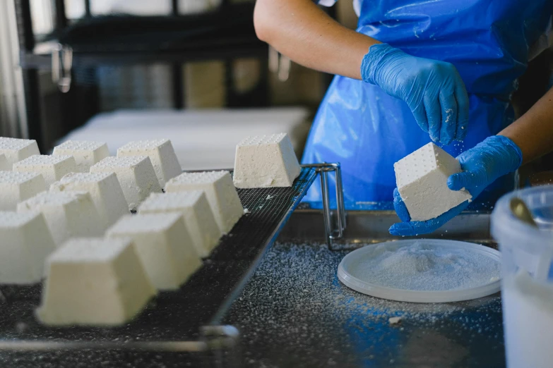 a person in a blue apron is making cubes of cheese, a marble sculpture, by Lee Loughridge, unsplash, cryogenic pods, industrial factory, avatar image, powdered sugar