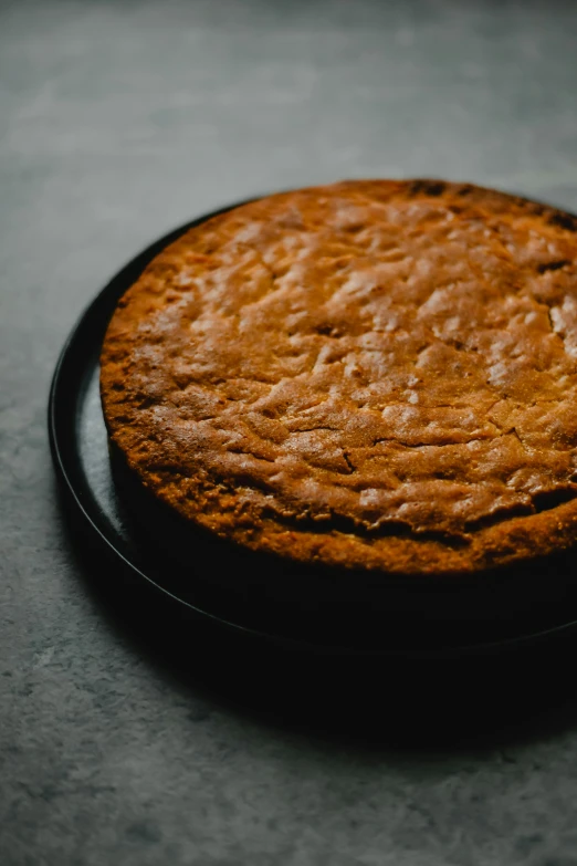 a cake sitting on top of a black plate, by Carey Morris, hurufiyya, vertically flat head, oak, cooked, utility