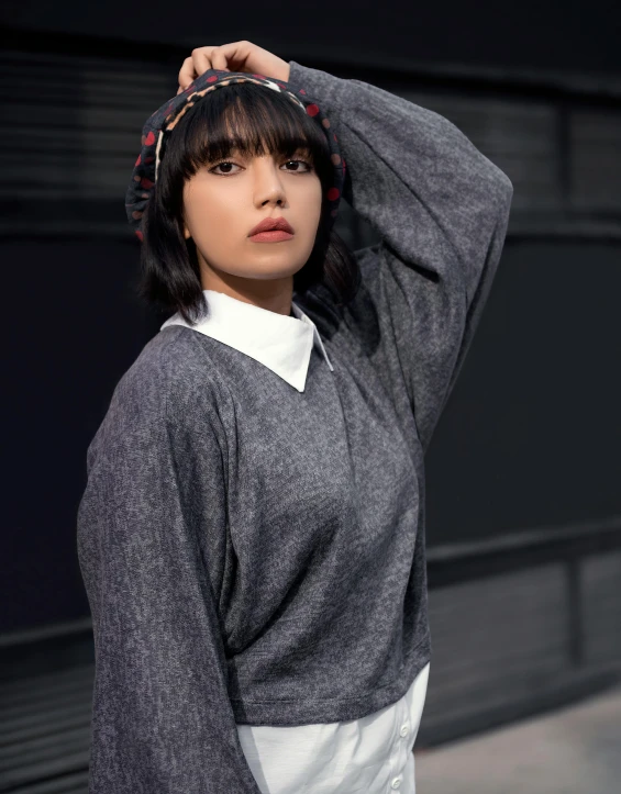 a woman posing for a picture in front of a building, grey sweater, non binary model, she has black hair with bangs, profile image