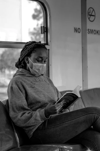 a woman sitting on a train reading a book, a black and white photo, by Sam Charles, pexels contest winner, wearing facemask, african woman, smoke :6, sitting on a couch