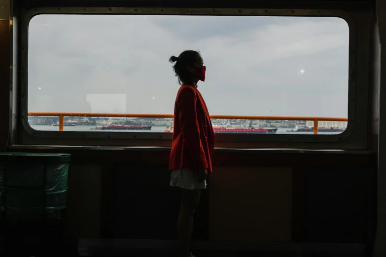 a person standing in front of a window looking out, standing on a ship deck, young asian girl, unsplash photography, wearing a mask