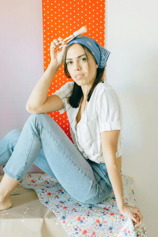 a woman sitting on top of a bed next to a wall, by Sara Saftleven, trending on pexels, pop art, bandana, aubrey plaza, light blues, in front of white back drop