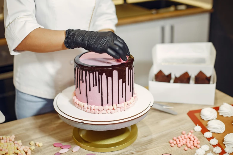 a woman is decorating a cake on a table, by Julia Pishtar, pexels contest winner, pink and black, fully chocolate, thick lining, thumbnail