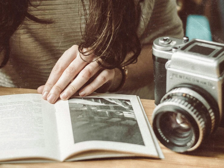 a person sitting at a table with a book and a camera, a picture, pexels contest winner, photorealism, lomography lady grey, scratches on photo, cute photograph, retro stylised