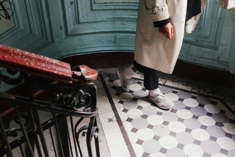 a woman standing in the corner of a room, a photo, inspired by Bourgeois, trending on unsplash, paris school, tiled floor, he is wearing a trenchcoat, wearing white sneakers, in front of the house