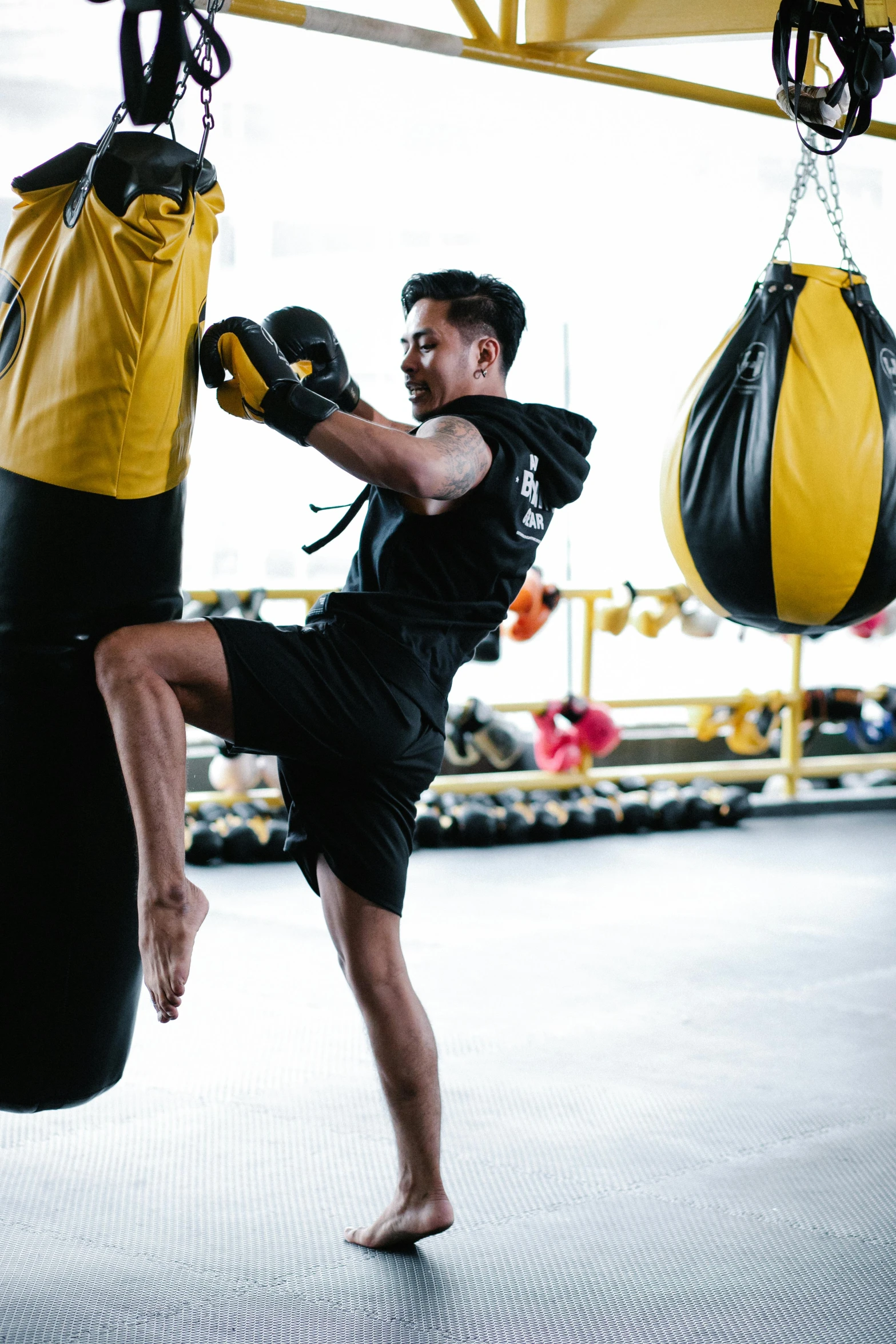 a man kicking a punching bag in a gym, by Robbie Trevino, black and yellow, manuka, square, high-quality photo
