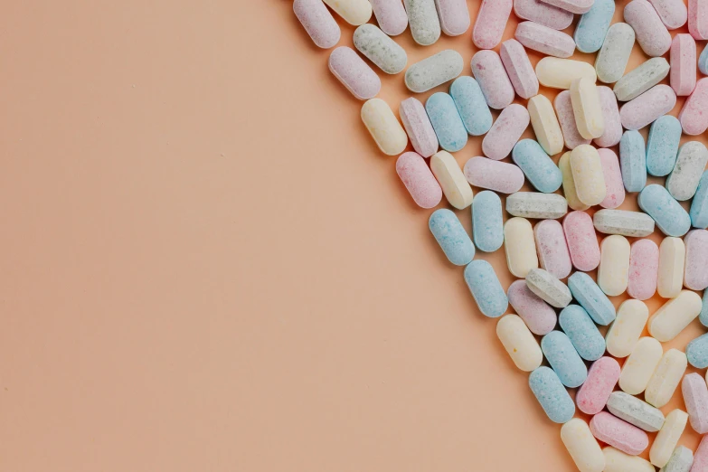 a pile of multicolored pills on a pink background, an album cover, trending on pexels, antipodeans, background image, frank moth, on grey background, orange pastel colors