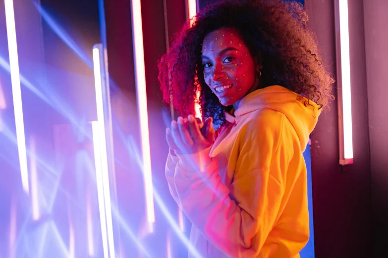 a woman in a yellow hoodie standing in front of neon lights, pexels contest winner, afro tech, led light strips, red and blue neon, black young woman