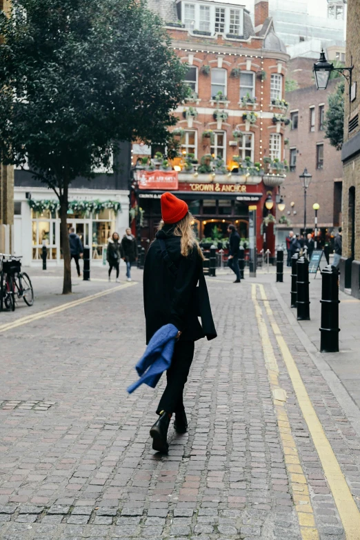 a woman walking down a street holding a blue umbrella, by Nina Hamnett, trending on unsplash, wearing a santa hat, london architecture, full body black and red longcoat, facing away