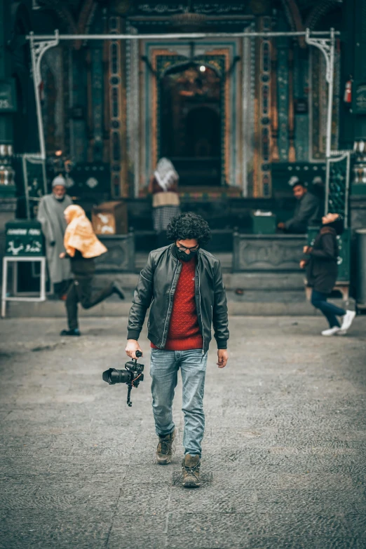 a man walking down a street holding a camera, red cinema camera, a man wearing a black jacket, top selection on unsplash, rugged