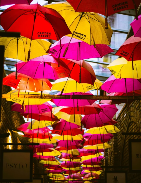 a street filled with lots of colorful umbrellas hanging from the ceiling, inspired by Jodorowsky, unsplash, hot pink and gold color scheme, in london, colorful”