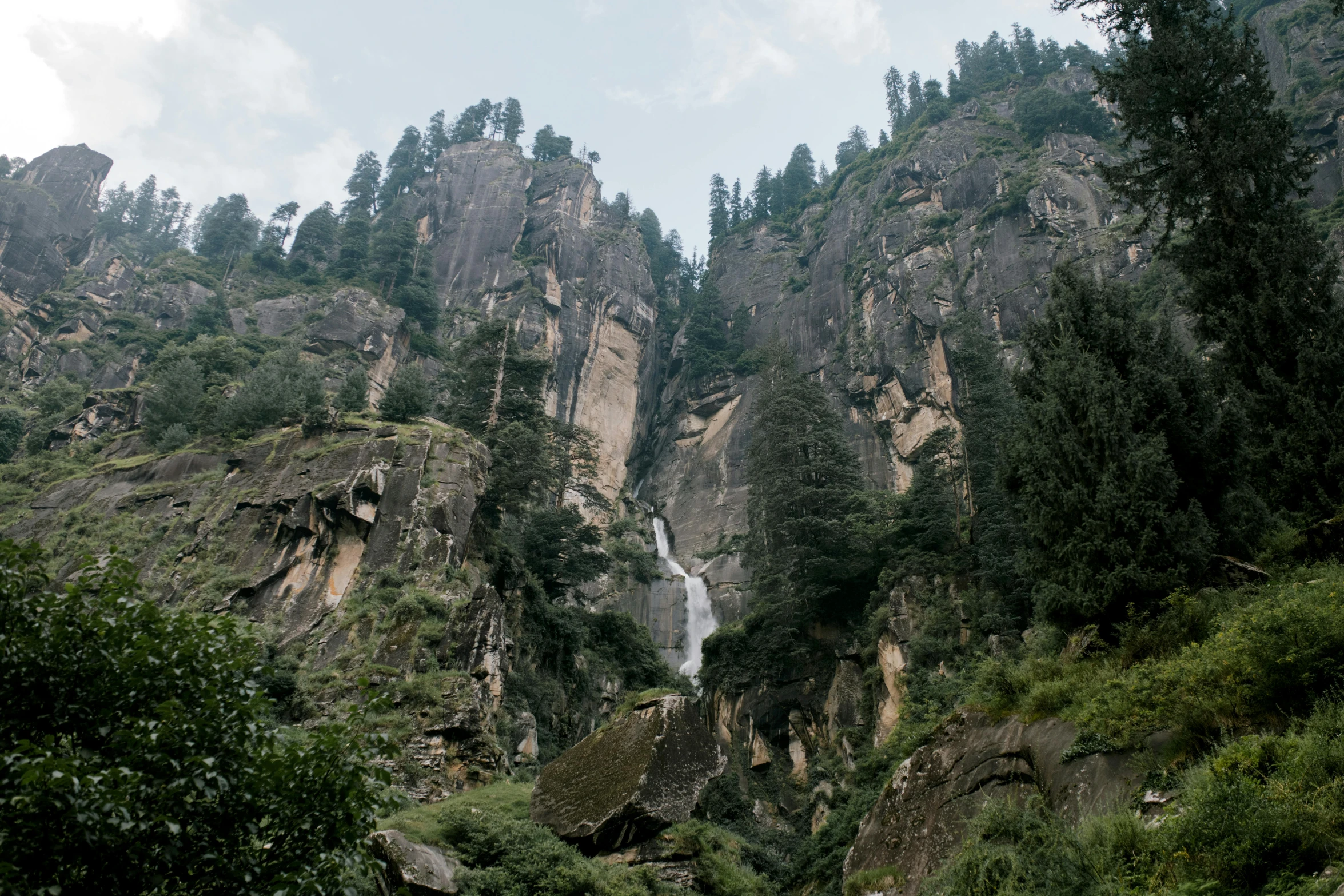 a group of people standing in front of a waterfall, by Muggur, pexels contest winner, hurufiyya, detailed trees and cliffs, uttarakhand, thumbnail, view from the ground