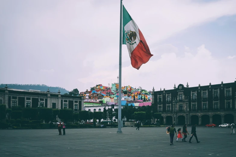 a mexican flag flying in front of a building, a photo, pexels contest winner, town square, avatar image, ground level shot, a group of people