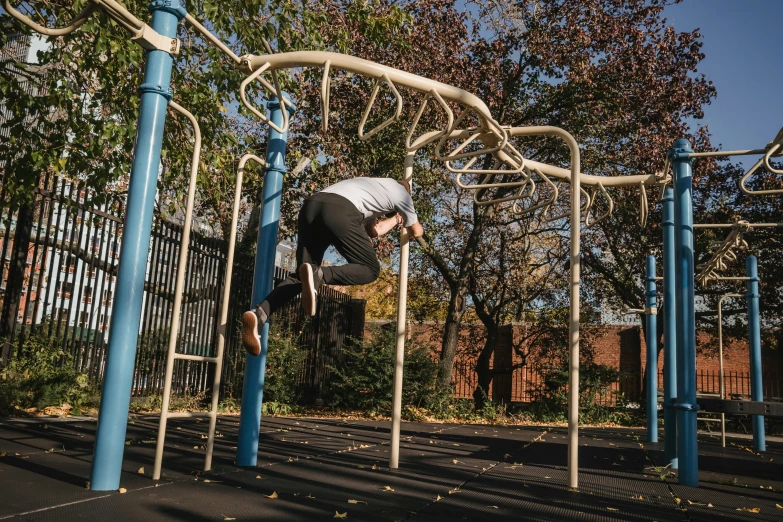 a man doing a trick on a monkey bars, a portrait, inspired by Ren Hang, unsplash, with a park in the back ground, structure : kyle lambert, tubular creature, fall season