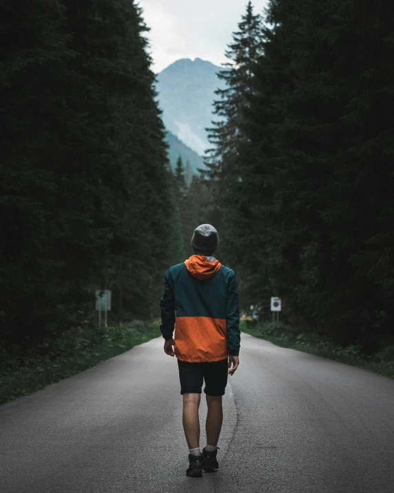 a man walking down a road in the middle of a forest, standing in front of a mountain, trending on vsco, dark grey and orange colours, wearing shorts