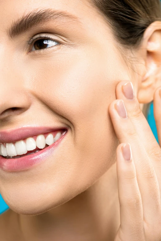 a close up of a person holding a toothbrush, beauty mark on cheek, with a blue background, welcoming grin, wide nostrils