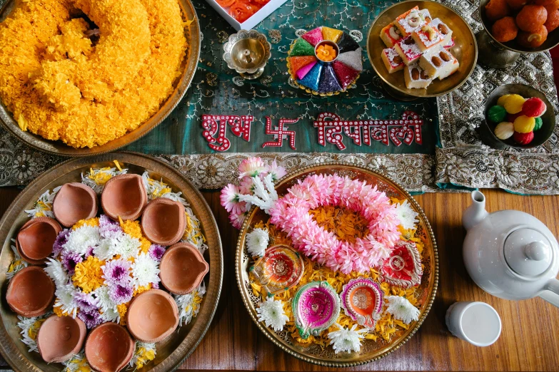 a table topped with plates of food on top of a wooden table, trending on unsplash, hurufiyya, hindu ornaments, bed of flowers on floor, celebration, sanskrit