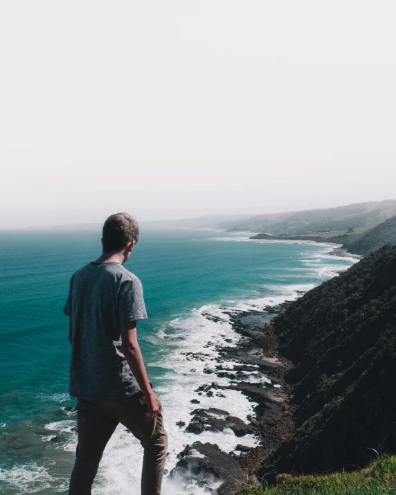 a man standing on a cliff overlooking the ocean, pexels contest winner, lgbtq, human staring blankly ahead, australian beach, a photo of a disheveled man