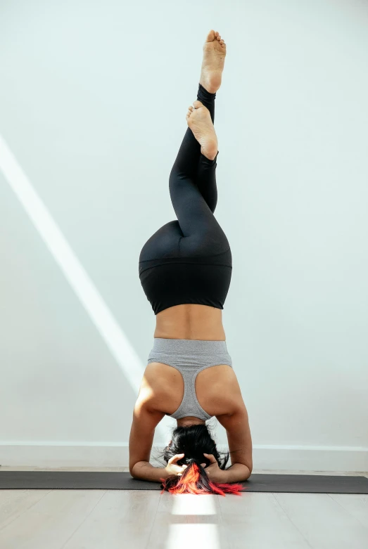a woman doing a handstand on a yoga mat, arabesque, wearing fitness gear, with a spine crown, grey, looking upwards