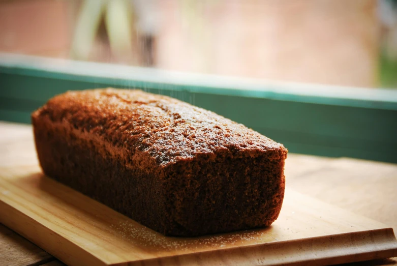 a loaf of bread sitting on top of a wooden cutting board, an album cover, unsplash, the greatest cake, brown, thick lining, view from side