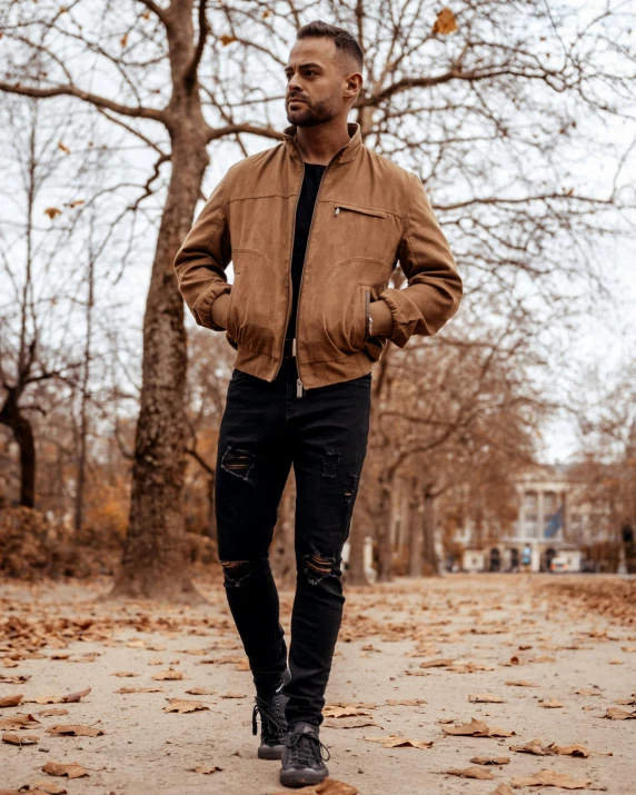 a man standing in a park with his hands in his pockets, an album cover, inspired by Theo Constanté, pexels contest winner, happening, dusty rown bomber leather jacket, brown:-2, thumbnail, lgbtq