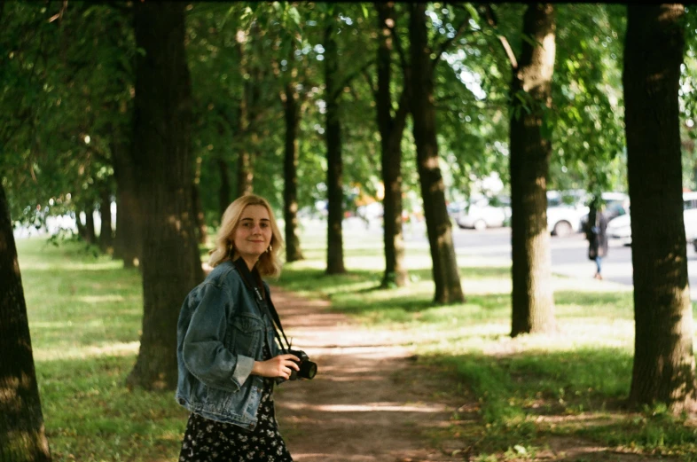 a woman standing on a path in a park, a picture, inspired by Elsa Bleda, pexels contest winner, photorealism, shot with a arriflex 35 ii, imogen poots, while smiling for a photograph, alexey gurylev