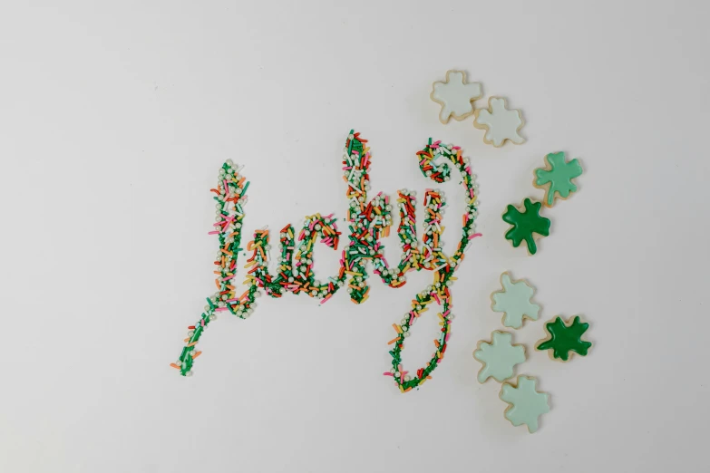 the word joy spelled in sprinkles on a white surface, a jigsaw puzzle, by Nicolette Macnamara, four leaf clover, ultra detailed wire decoration, taken with kodak portra, hand