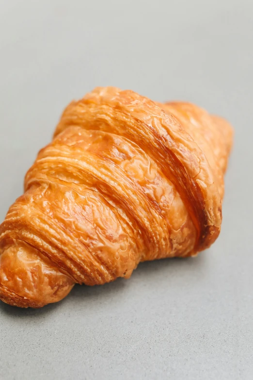 a close up of a croissant on a table, on a gray background, caparisons, detailed product image, 3/4 front view