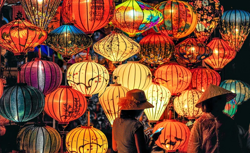 a woman standing in front of a display of lanterns, a colorized photo, pexels contest winner, square, mai anh tran, rich vivid vibrant colors, colorful crowd