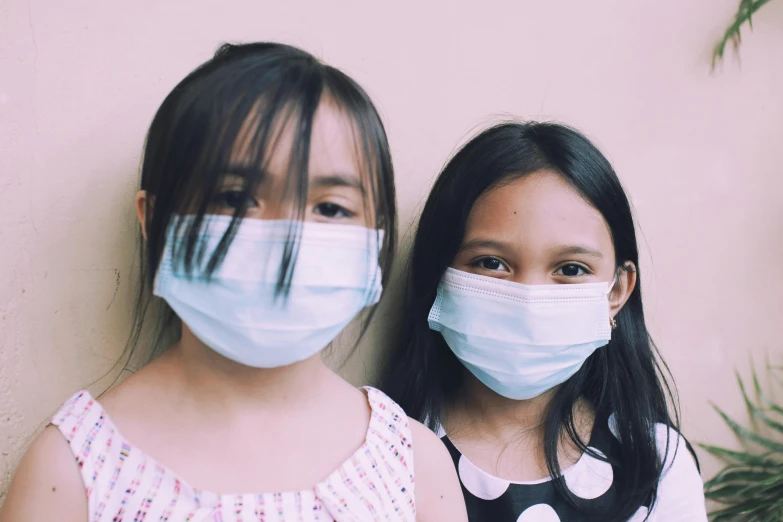a couple of young girls standing next to each other, pexels contest winner, medical mask, south east asian with round face, contaminated, diy