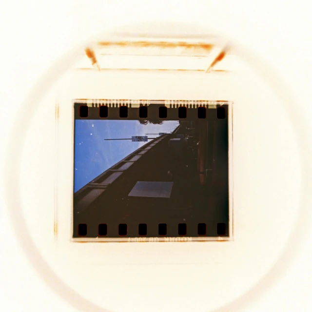 a close up of a film strip with a building in the background, a polaroid photo, inspired by László Moholy-Nagy, video art, alien invasion. 2 4 mm, inside a glass jar, high angle camera, camera looking up