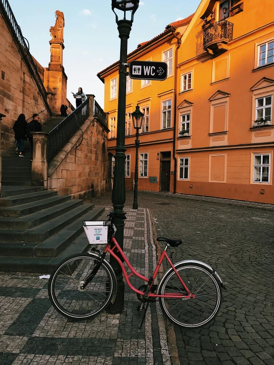 a red bike parked next to a lamp post, by Matija Jama, prague in the background, 🚿🗝📝, profile image