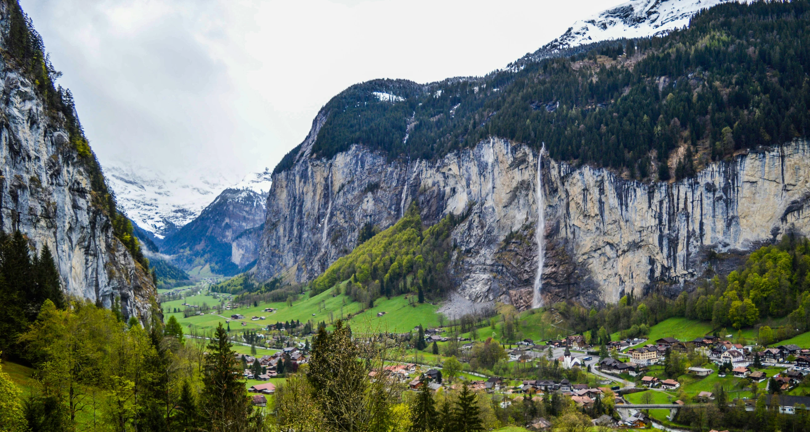 a view of a valley with a mountain in the background, by Daniel Seghers, pexels contest winner, renaissance, lauterbrunnen valley, slide show, with trees and waterfalls, urban surroundings