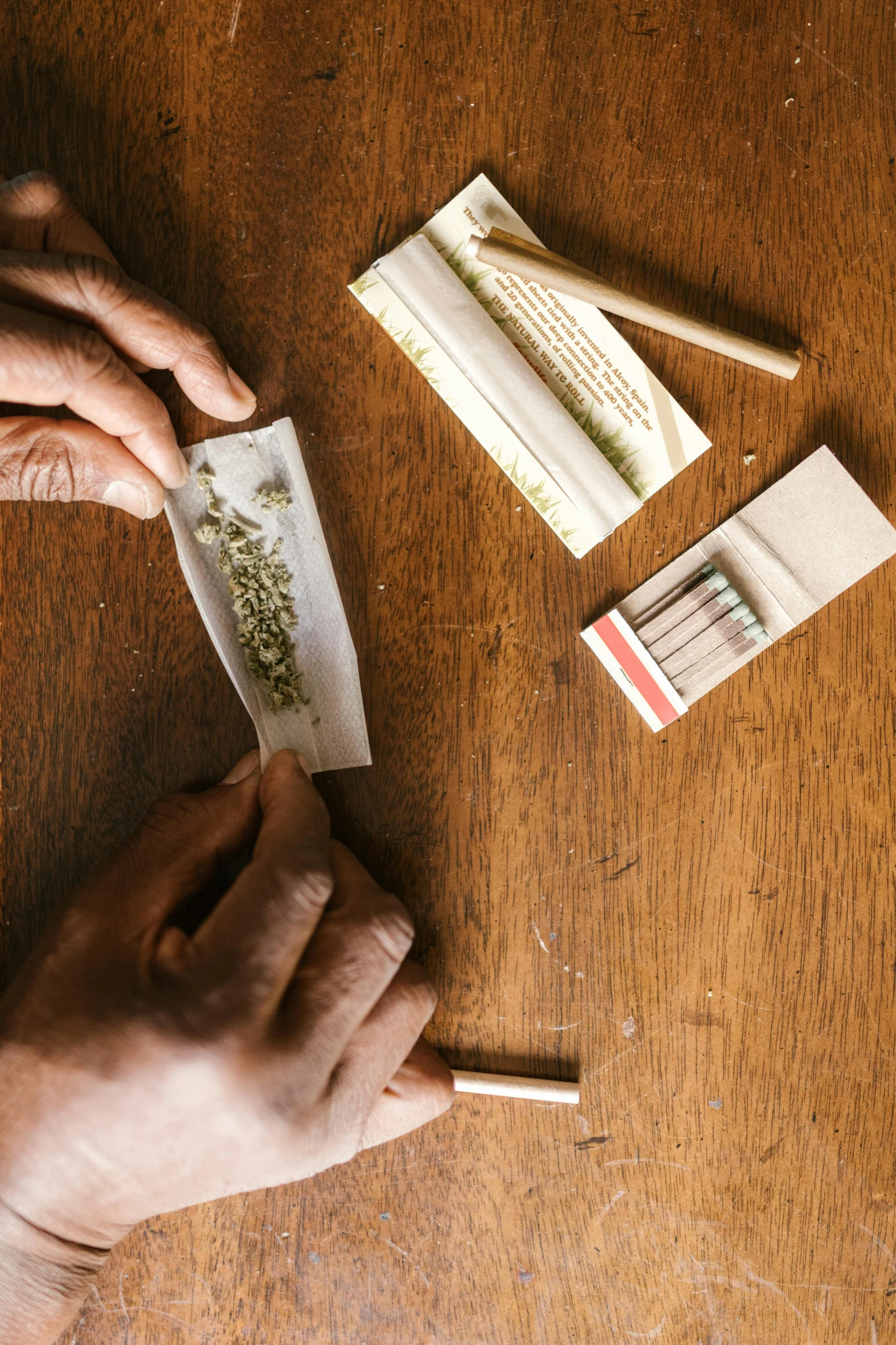 a person cutting a piece of paper on top of a wooden table, cigarrette boxes at the table, pot leaf, profile image