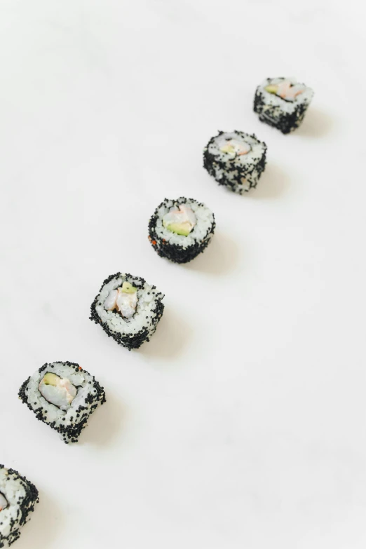 sushi rolls arranged in a row on a white surface, inspired by Maki Haku, unsplash, mingei, mother of pearl iridescent, almost black, 6 pack, sugar sprinkled