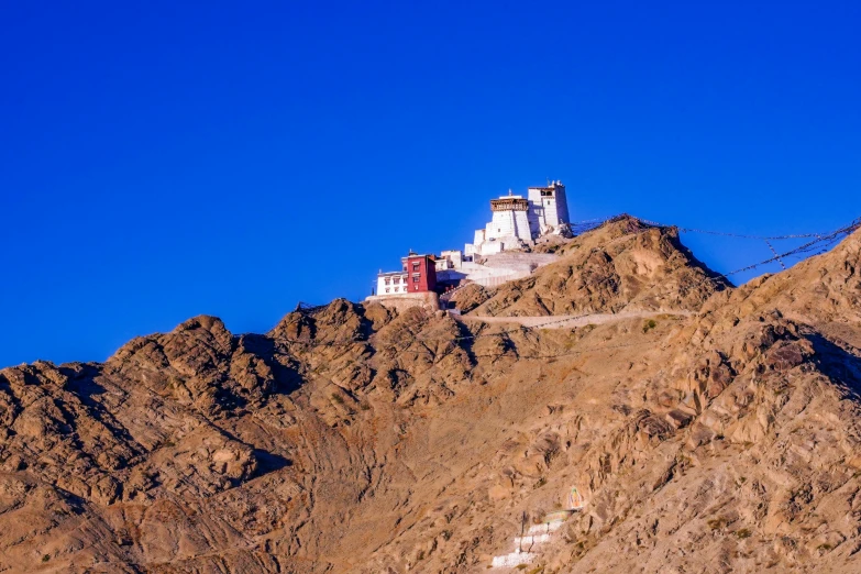 a large white building sitting on top of a mountain, pexels contest winner, clear blue skies, india, avatar image, brown