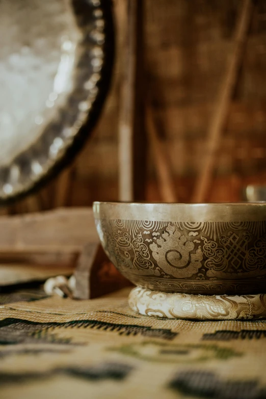 a bowl sitting on top of a table next to a mirror, an album cover, inspired by Li Di, trending on unsplash, renaissance, a beautiful buddhist mandala, etched inscriptions, brass horns, silver，ivory