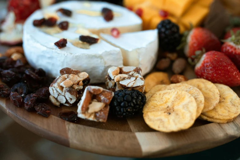 a wooden plate topped with cheese, fruit and crackers, a close up shot, offering a plate of food, close shot, date