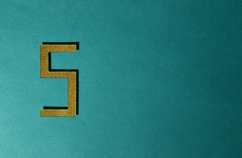 a close up of a letter e on a blue surface, an album cover, hypermodernism, gold and teal color scheme, mp5s, background image, 5