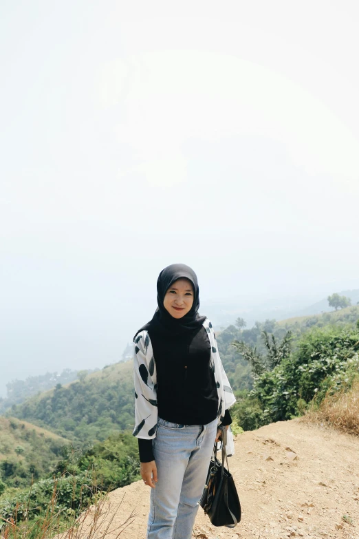 a woman standing on top of a dirt road, a picture, inspired by JoWOnder, sumatraism, white hijab, with black, in the hillside, slightly pixelated